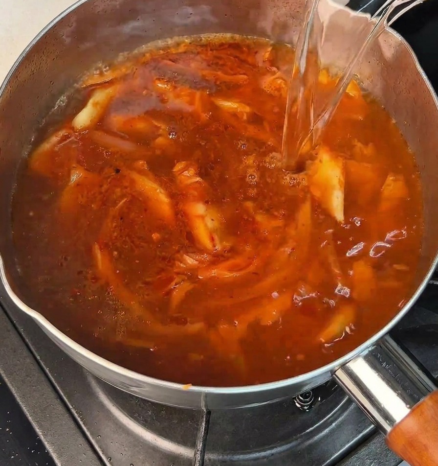 Un chorro de agua hirviendo vertiéndose en una olla con una base roja picante que burbujea.