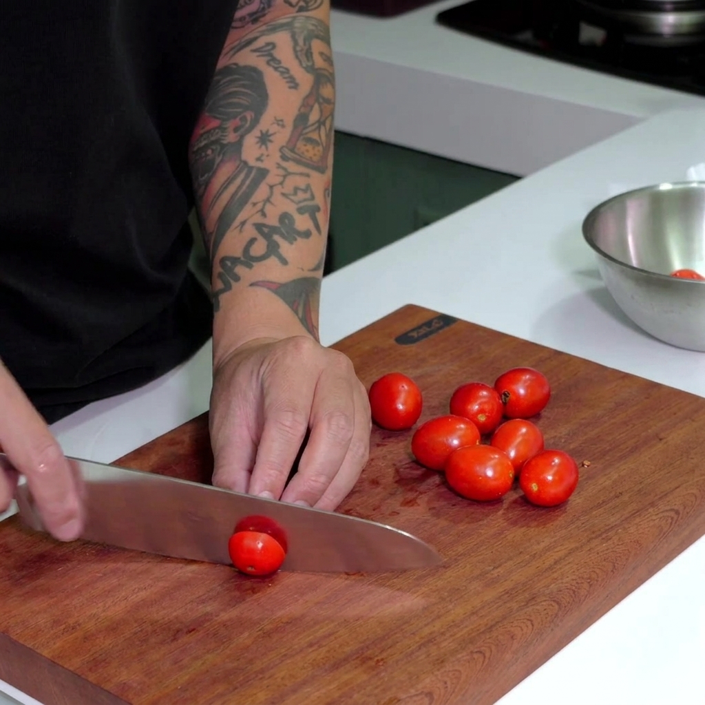 Cuchillo de chef cortando tomates cherry rojos brillantes sobre una tabla de madera oscura.