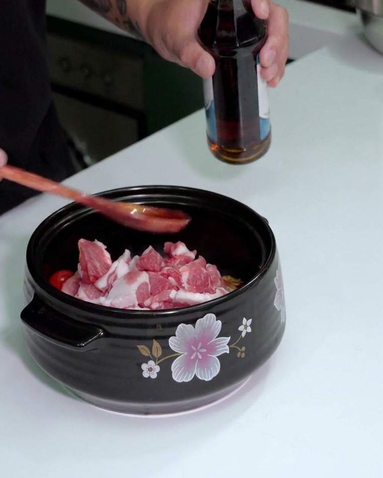 Persona vertiendo salsa de pescado desde una botella en una cuchara de madera sobre la olla.