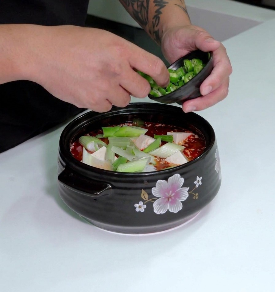 Chiles verdes laminados siendo espolvoreados desde un pequeño cuenco sobre la sopa con tofu y puerros.