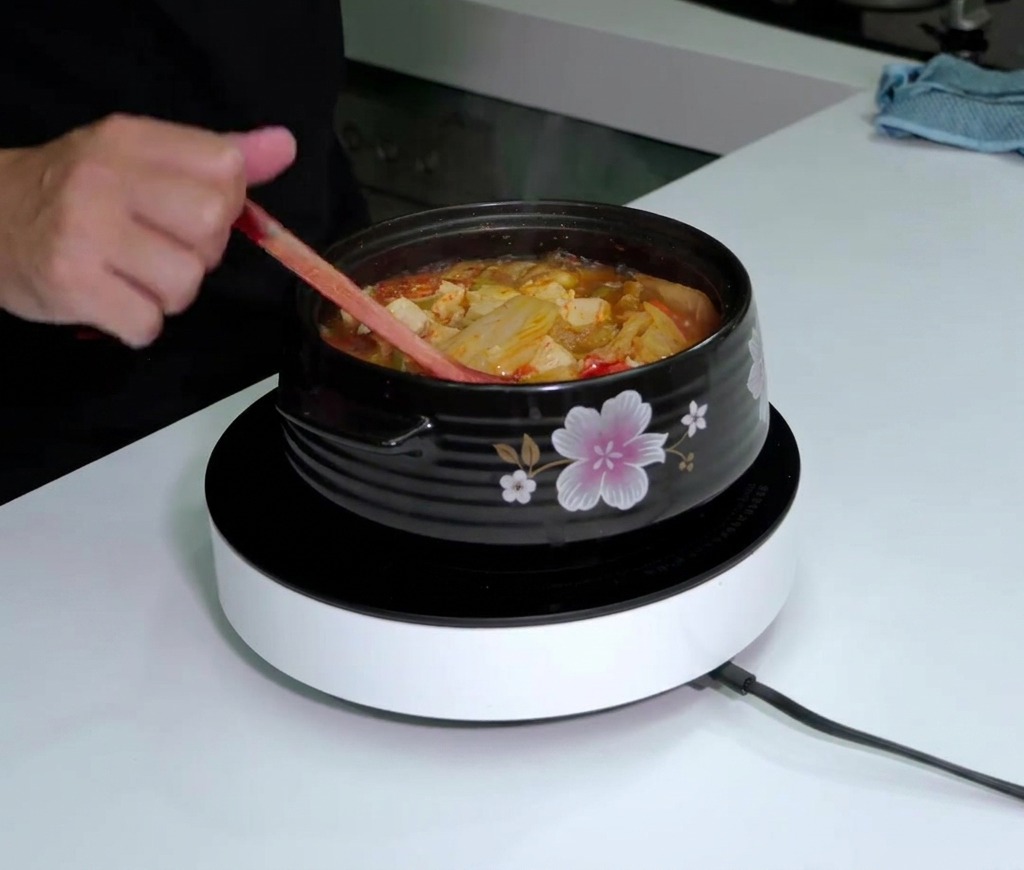 Botella de salsa Tabasco sobre una olla humeante de sopa de kimchi roja mientras se remueve.