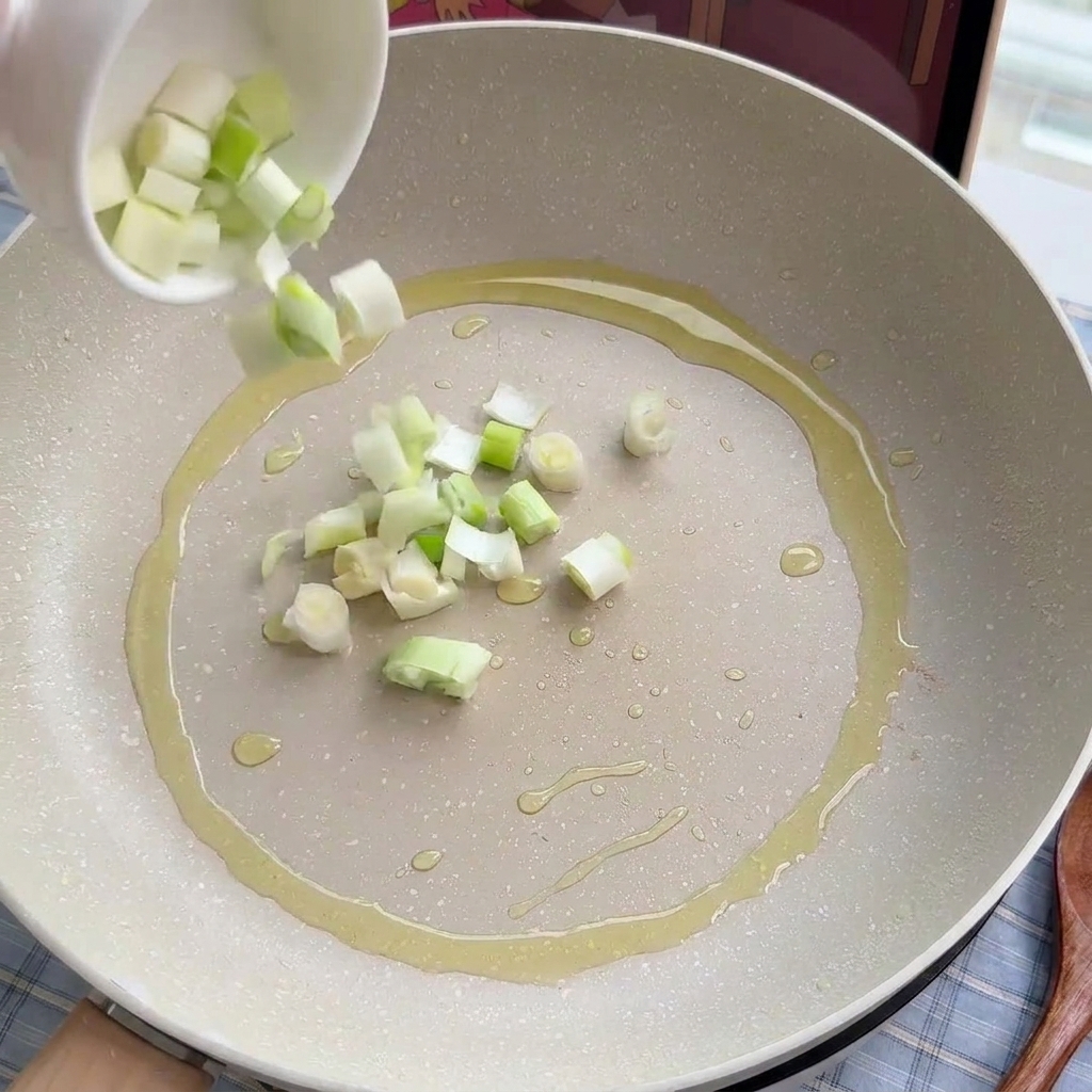 Cebolletas y puerros picados siendo sofritos suavemente en una sartén con aceite.