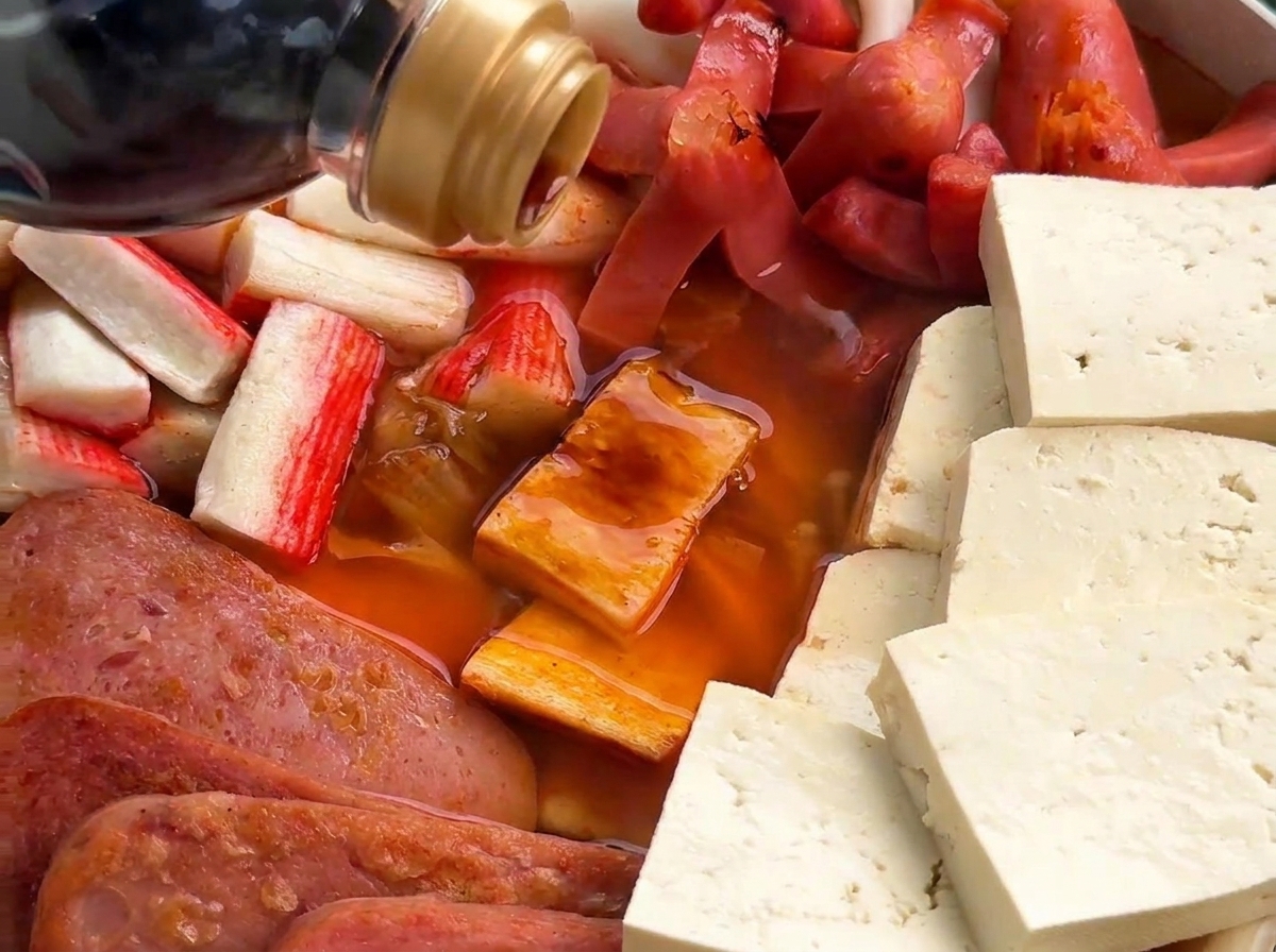 Plano detalle de salsa de soja oscura cayendo en una olla con salchichas y carne en un caldo rojizo.