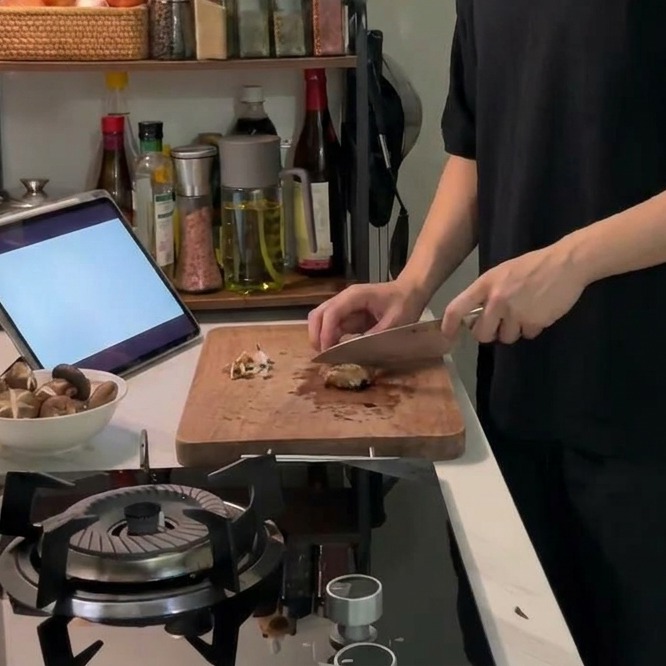 Un cuchillo afilado marcando un patrón de cruz decorativo en la parte superior de un champiñón shiitake sobre una tabla de cortar.