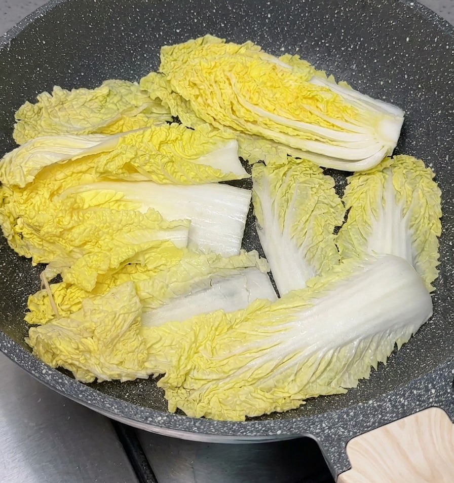 Trozos de col china verde y amarilla cubriendo el fondo de una olla gris antiadherente.
