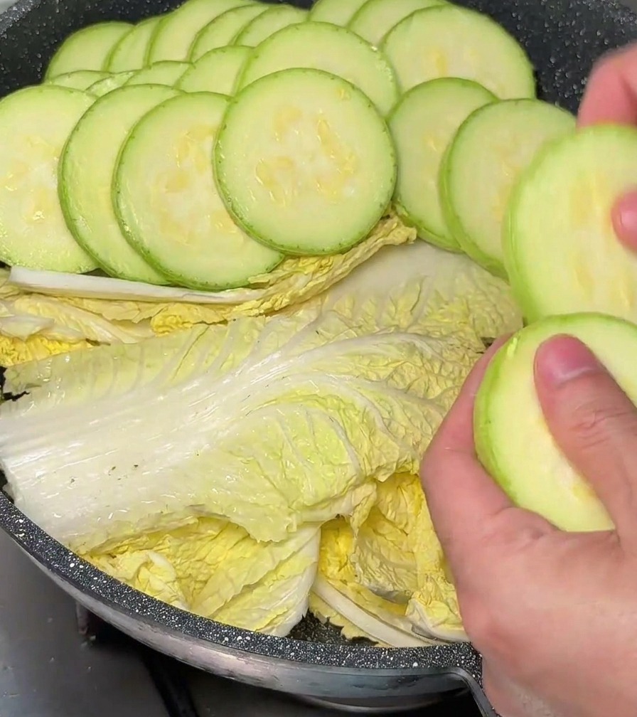 Manos colocando rodajas de calabacín de forma circular sobre la col en una olla.