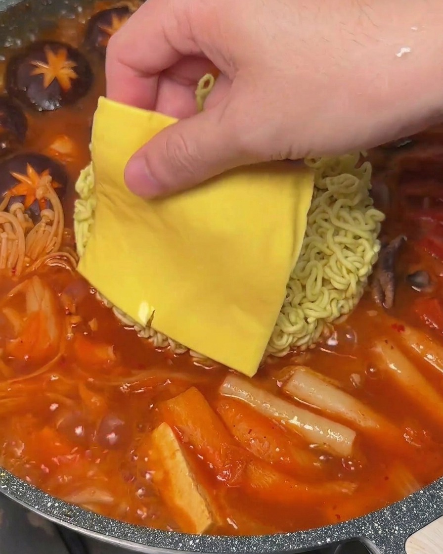 Una loncha de queso amarillo sobre los fideos ramen en una olla de estofado coreano.