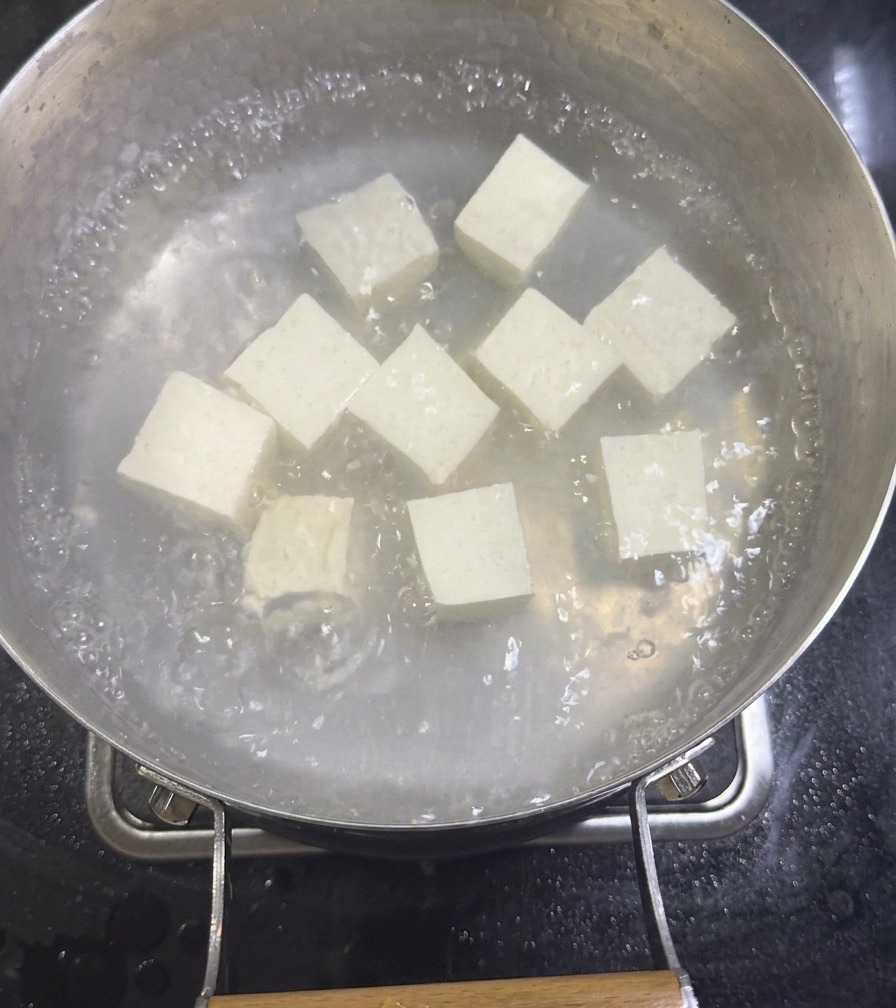 Cubos de tofu sedoso blanco hirviendo a fuego lento en una olla con caldo de almejas diluido.