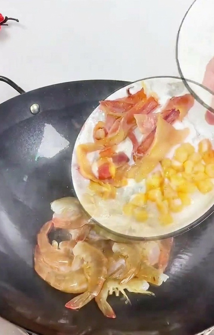 Una persona vertiendo calamar troceado y vieiras secas en un wok con gambas y tiras de jengibre.