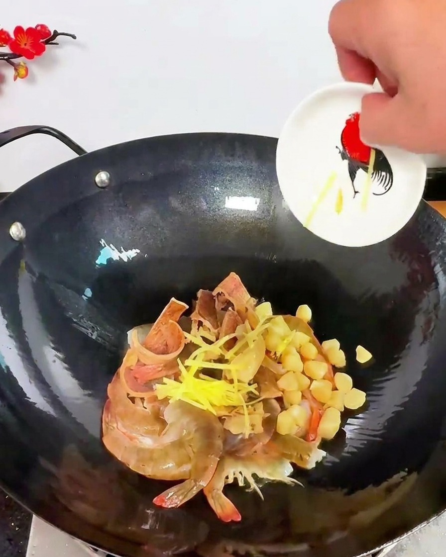 Tiras de jengibre amarillo esparcidas sobre una mezcla de gambas y vieiras secas en un wok oscuro.