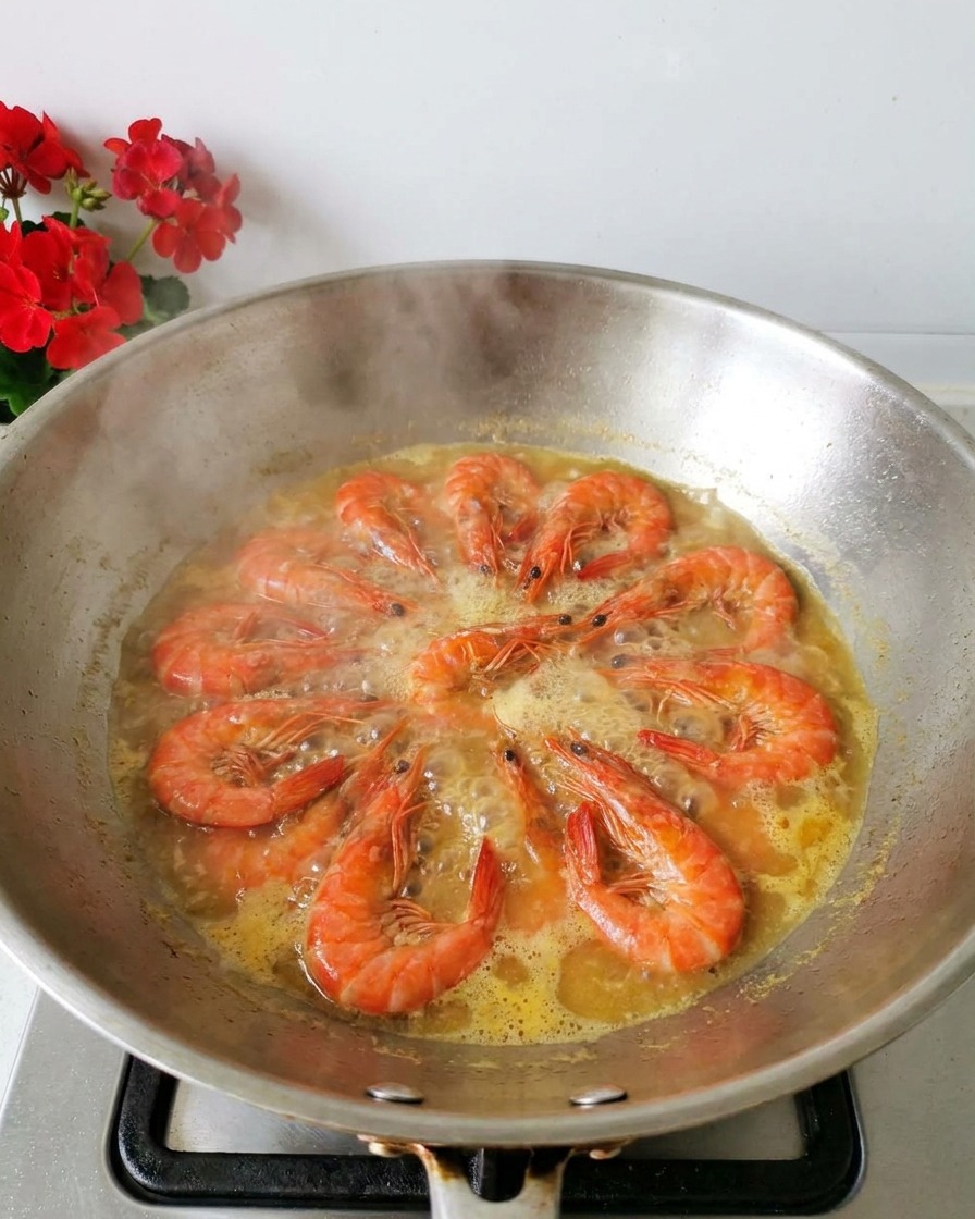 Gambas naranjas hirviendo en un caldo amarillento dentro de un wok de acero inoxidable con vapor subiendo.
