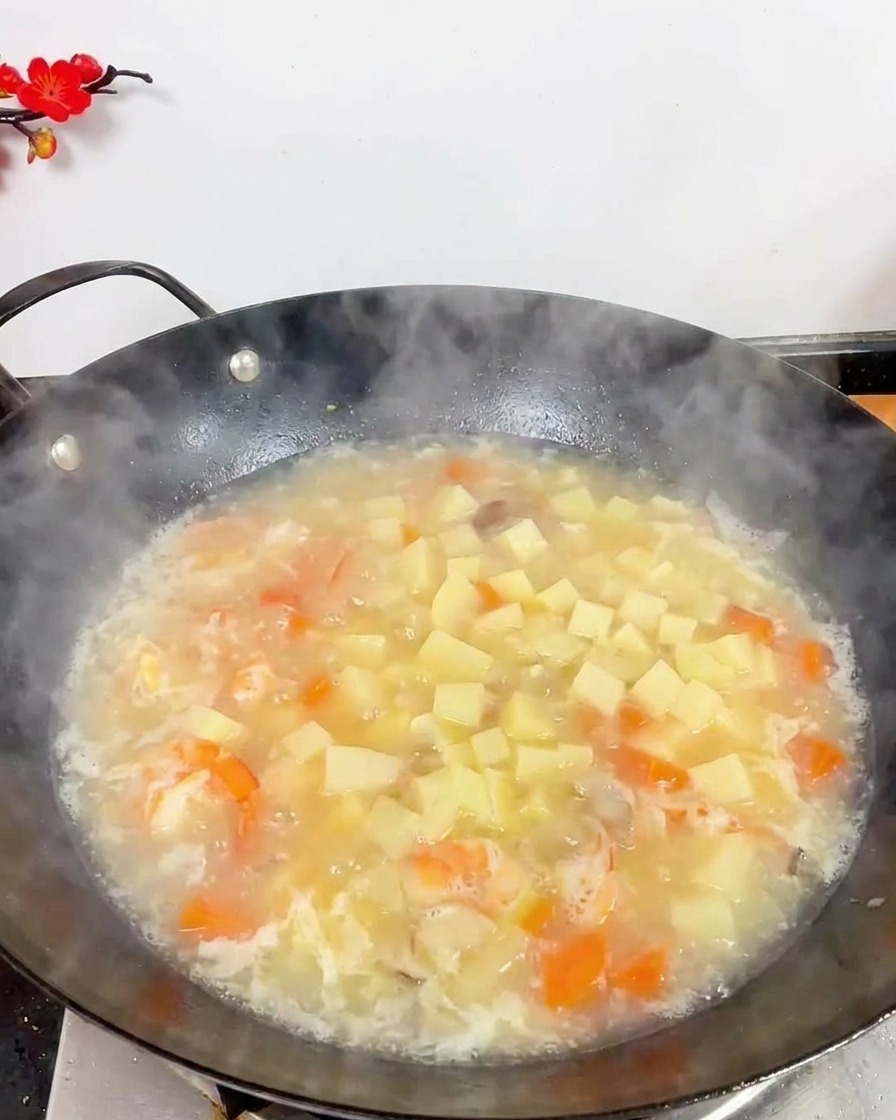 Vista superior de un wok con sopa blanca hirviendo, con muchos dados de tofu, gambas y pequeñas setas marrones.