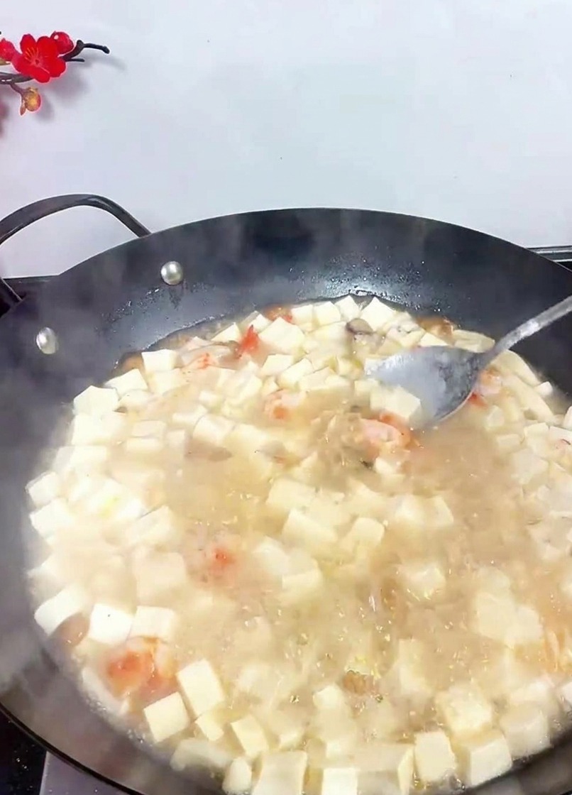 Una cuchara removiendo un wok burbujeante de sopa blanca de tofu para incorporar los condimentos.