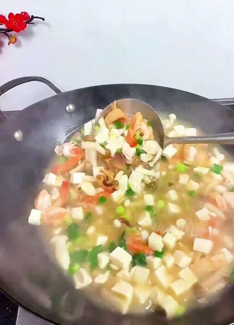 Un cazo metálico mezclando dados de tofu, gambas y hierbas verdes en un wok humeante.