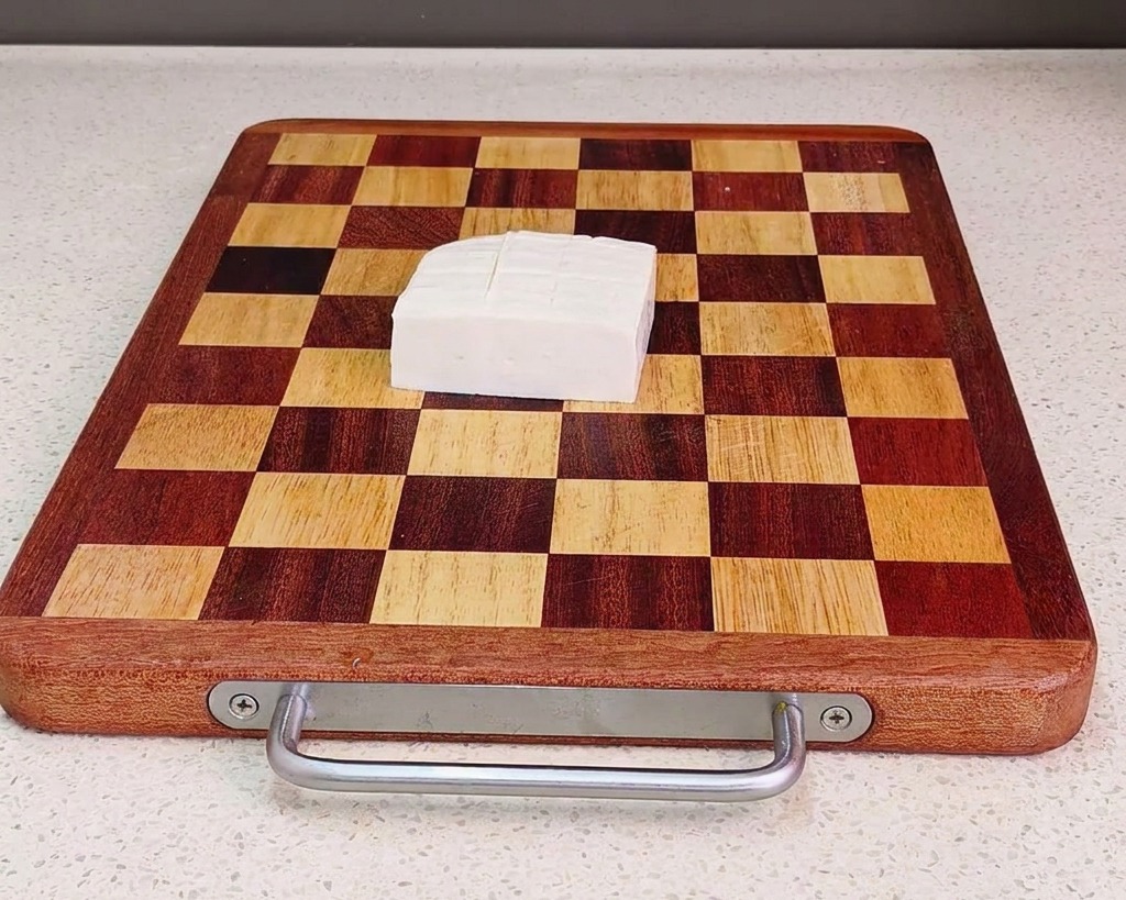 Bloque de tofu blanco cortado en cubos uniformes sobre una tabla de cortar de madera.
