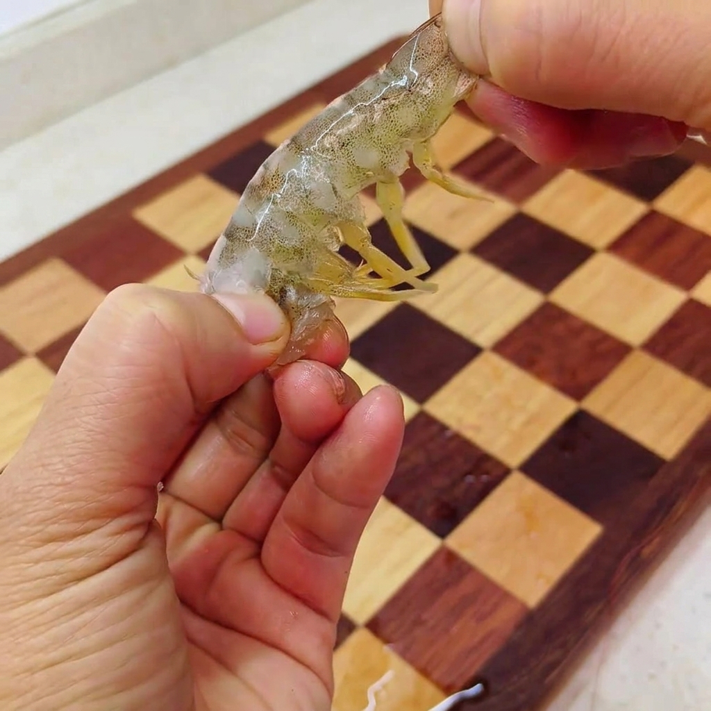 Manos pelando un langostino crudo y sacando la carne de la cola sobre una tabla de madera.