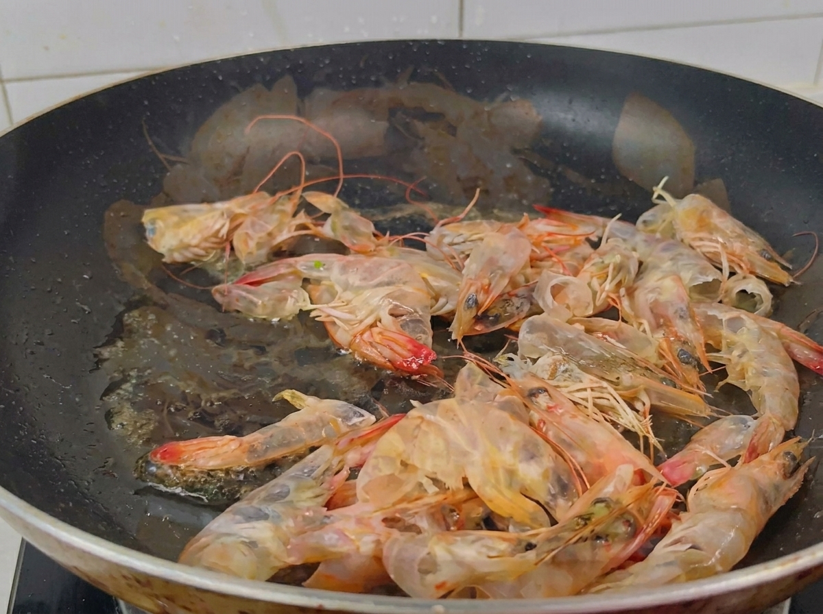 Sartén negra con cáscaras de langostino tornándose naranjas mientras se sofríen en aceite.