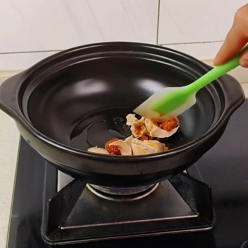 Espátula removiendo trozos de huevo de pato salado en una olla de barro hasta que espuman.