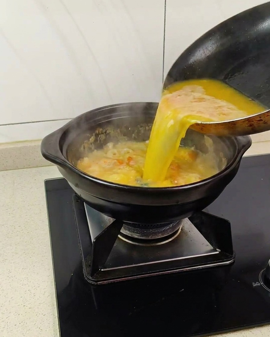 Vertiendo el caldo de langostino dorado en una olla de barro con la base de yema espumosa.