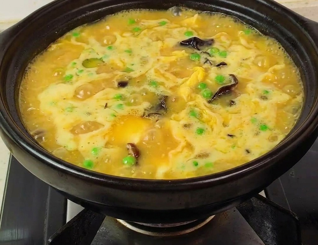Sopa espesa y burbujeante con langostinos rosas y guisantes en una olla de barro lista para comer.
