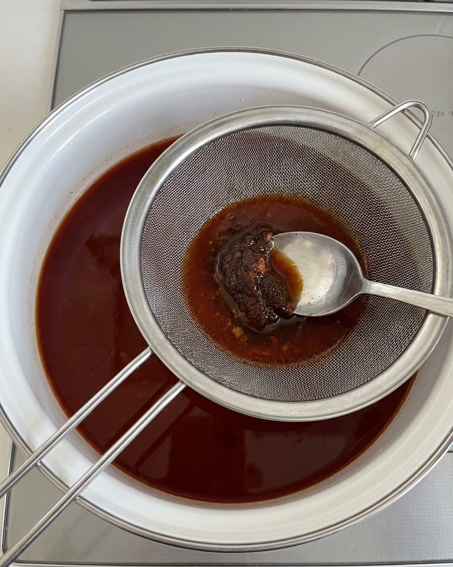 Usando una cuchara para presionar pasta de soja espesa a través de un colador metálico sobre el caldo hirviendo.