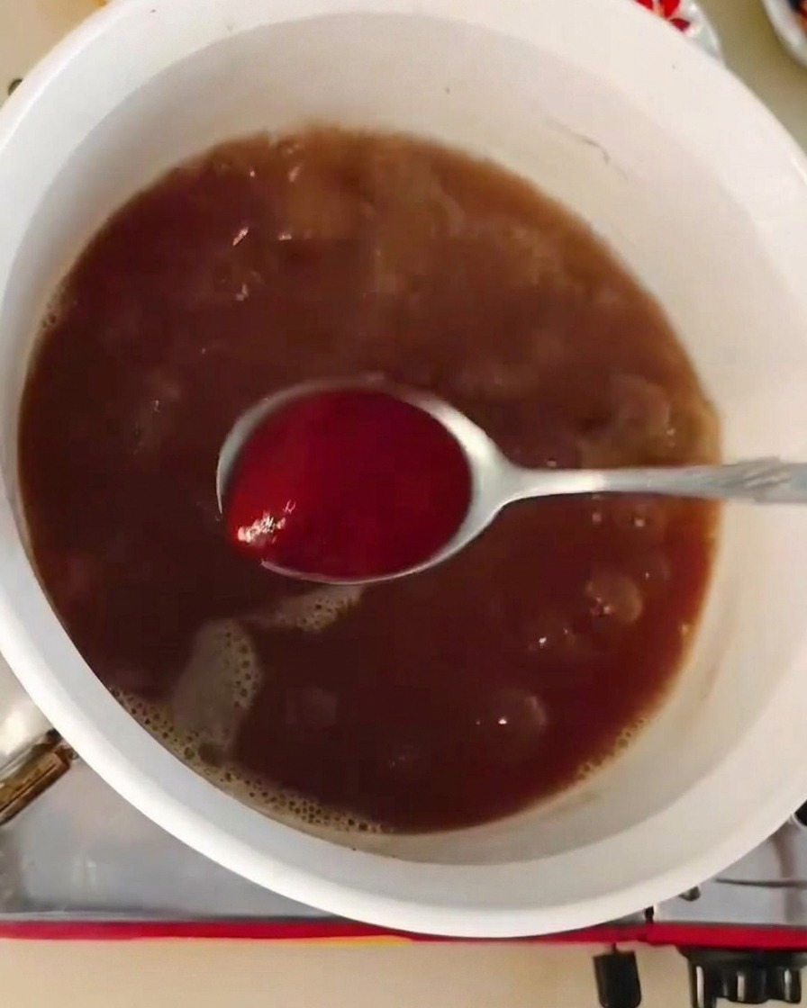 Una cucharada de pasta de chile rojo siendo incorporada a una olla de caldo marrón burbujeante.