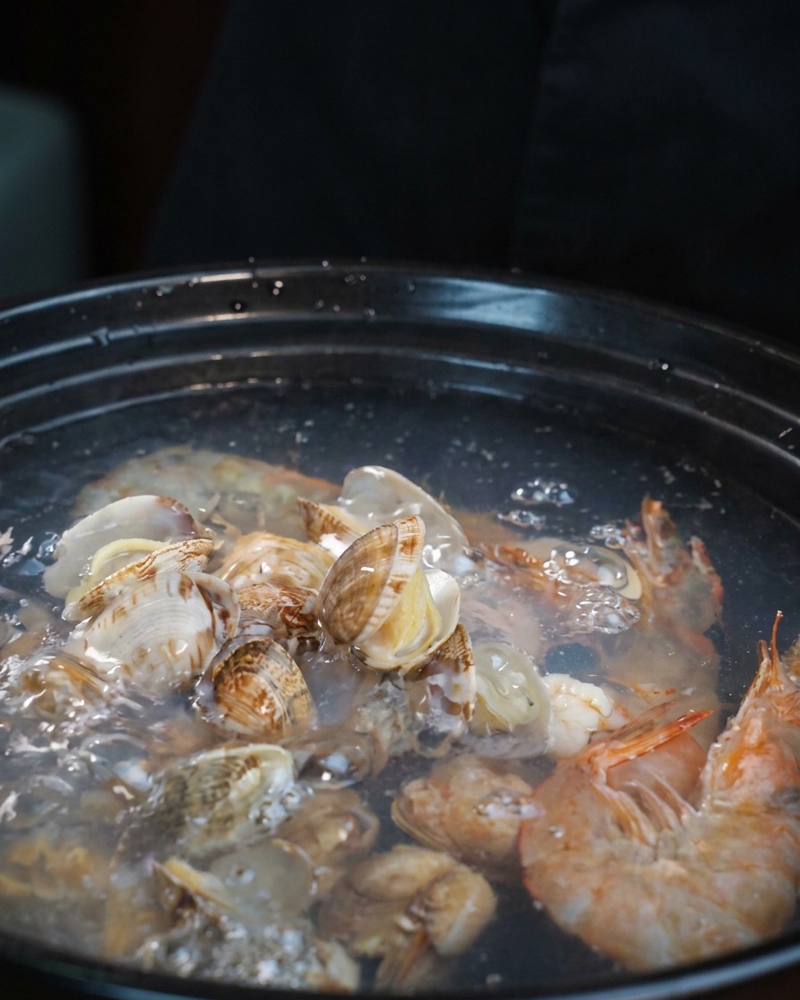 Trozos pálidos de tentáculos de pulpo crudo siendo añadidos a la olla de sopa de mariscos hirviendo.