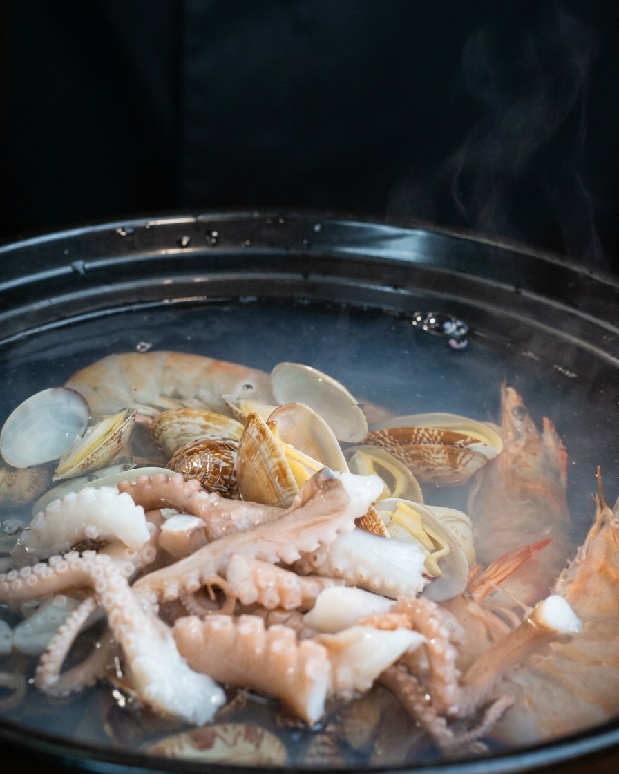Láminas de tofu blanco colocadas sobre el pulpo y las almejas en la olla a fuego lento.