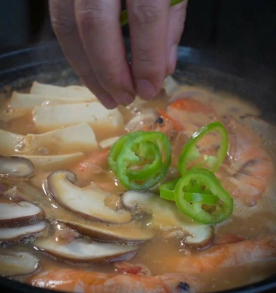 Aros de pimiento verde cayendo en una olla burbujeante de sopa de mariscos y pasta de soja.