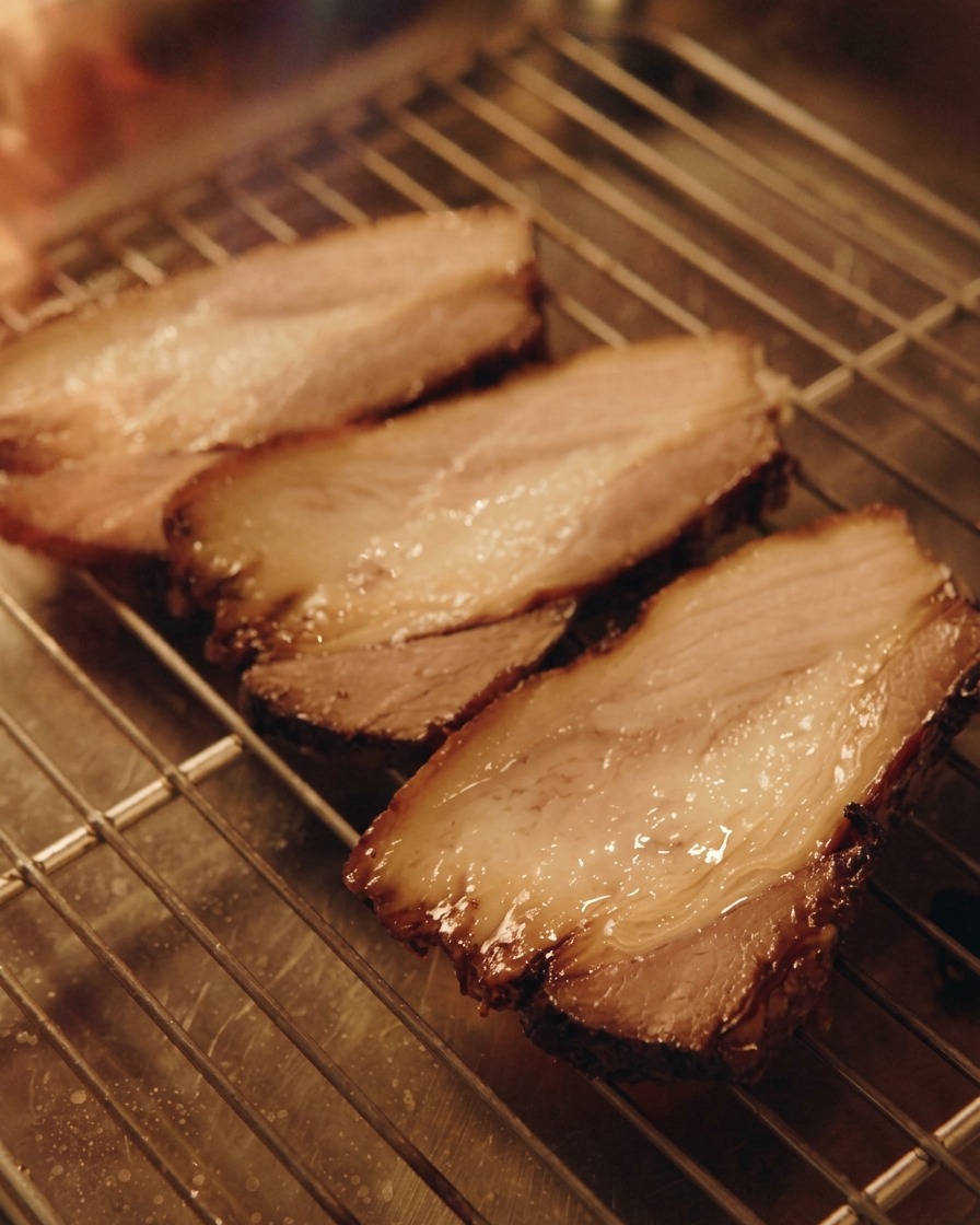 Un soplete de cocina dorando tres rebanadas gruesas de chashu de cerdo que reposan sobre una rejilla de metal.