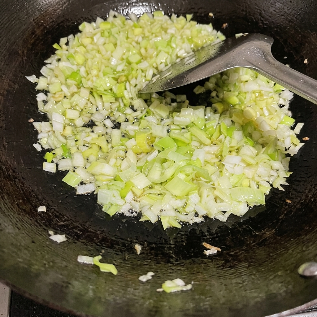 Cebolletas verdes picadas siendo salteadas en un wok negro con aceite y una espátula de metal.