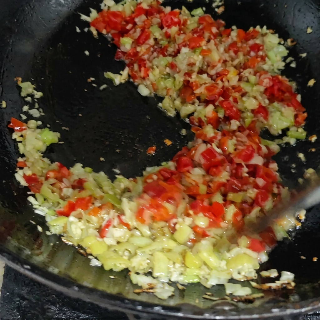 Mezcla colorida de chiles rojos y verdes picados salteándose con otros aromáticos en una sartén caliente.