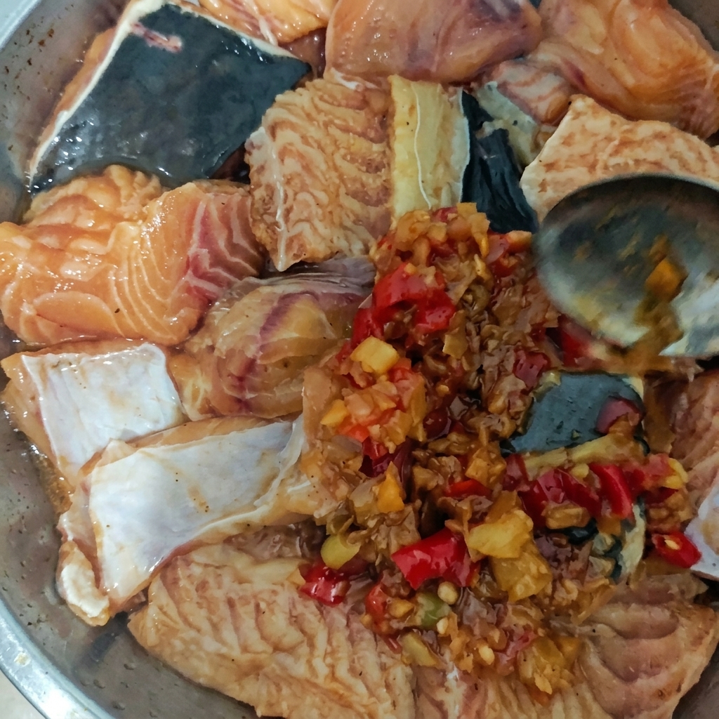 Plato de metal con trozos de pescado crudo siendo cubiertos con una salsa espesa de chile y ajo con una cuchara.