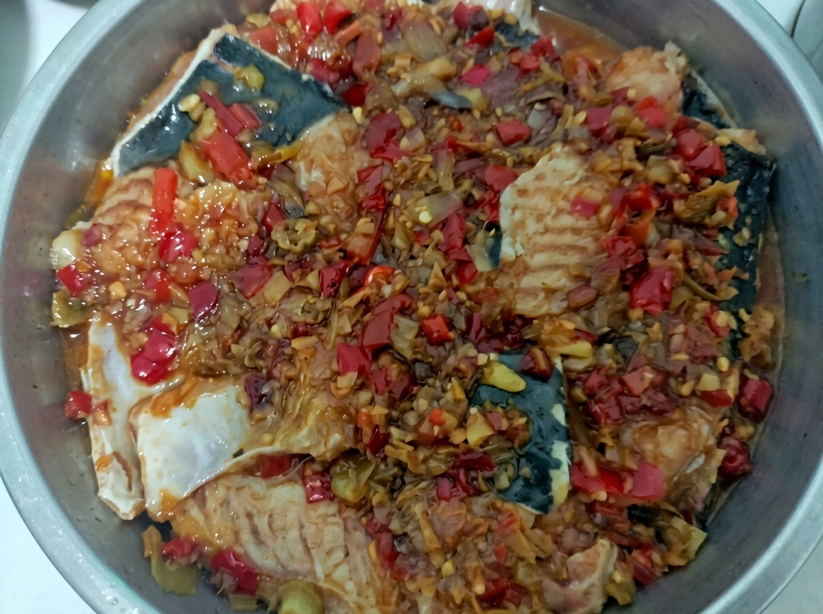 Bandeja de vapor de acero inoxidable con trozos de pescado blanco cubiertos por una vibrante salsa roja de chile.
