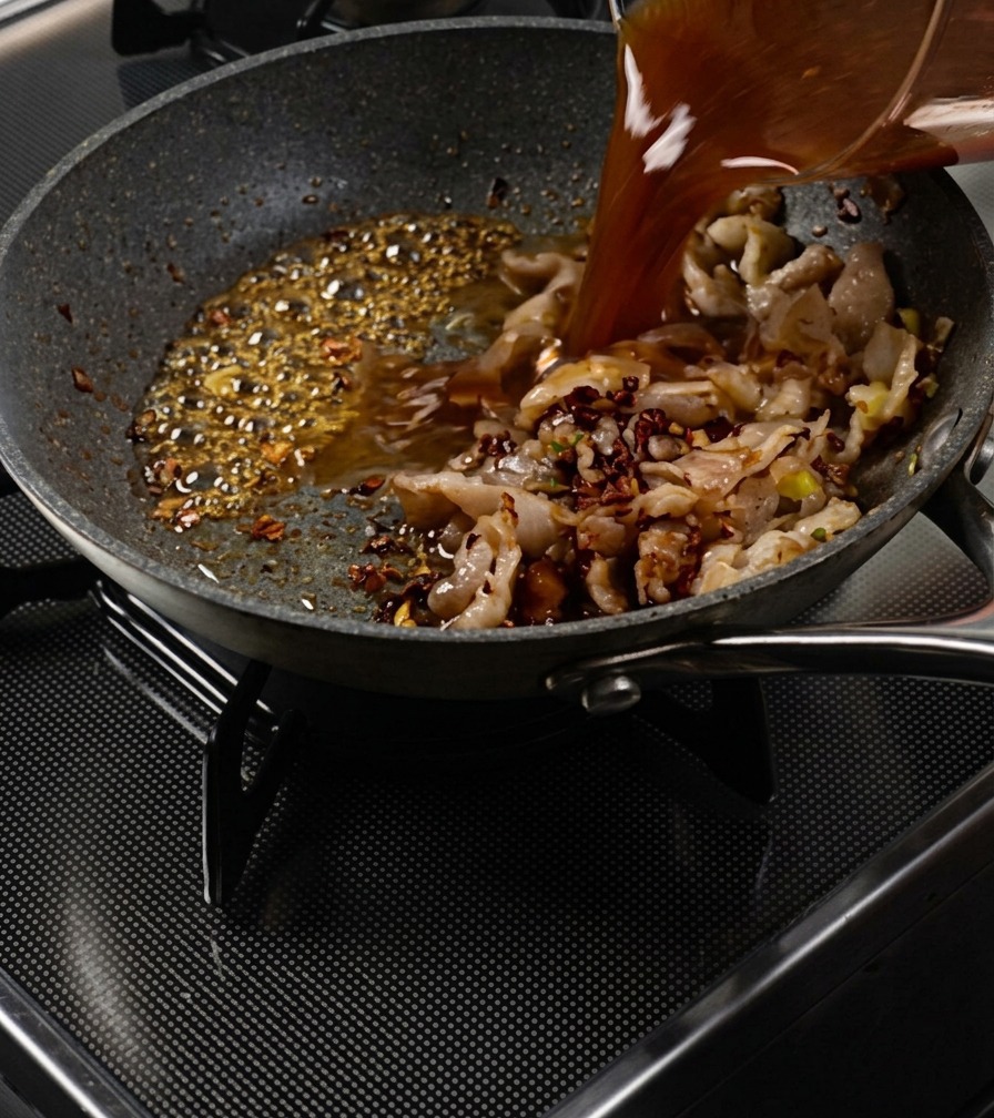Salsa marrón vertiéndose desde una jarra medidora en una sartén con cerdo salteado y caramelo burbujeante.