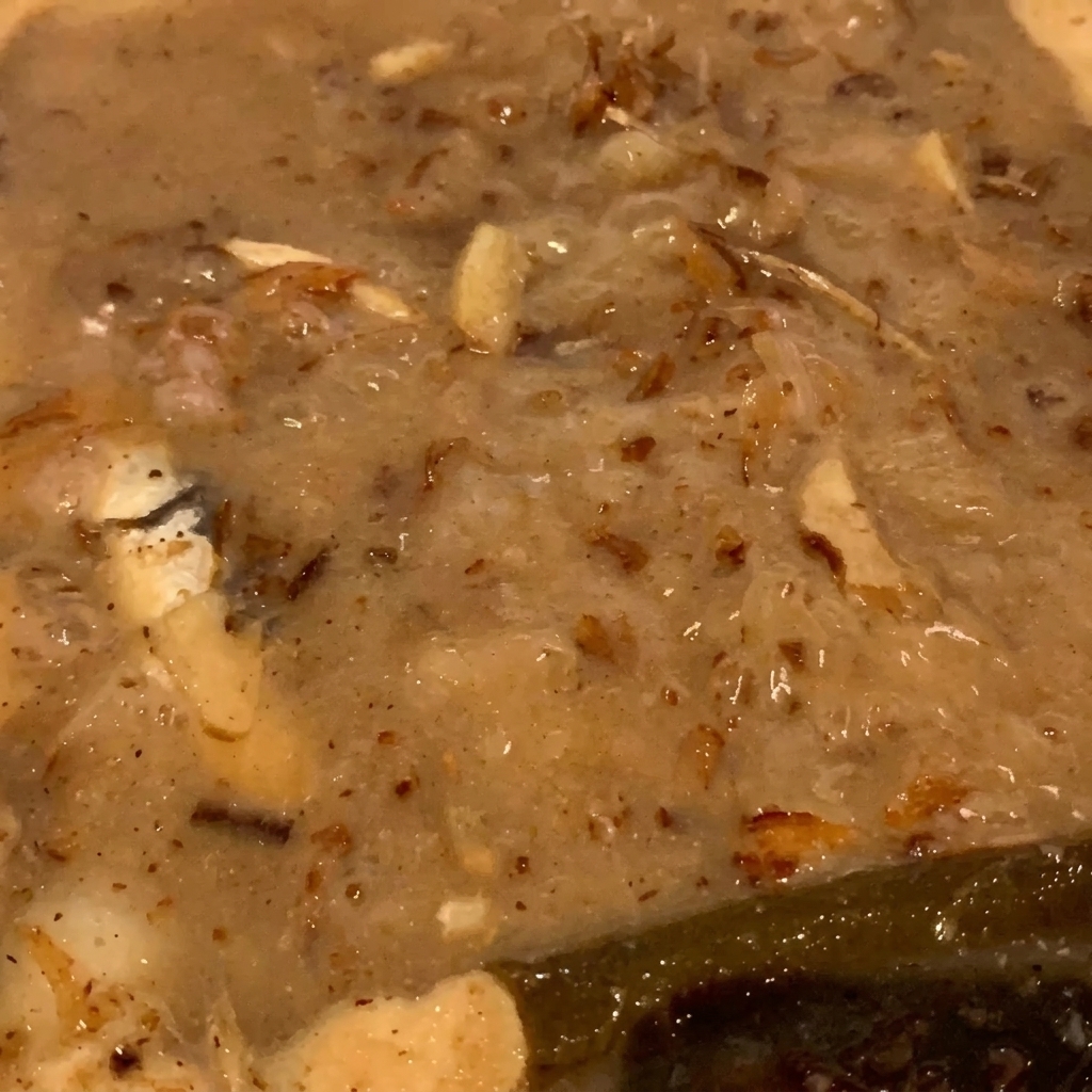 Primer plano de copos de pescado seco y pescaditos burbujeando dentro de un líquido espeso de color canela.