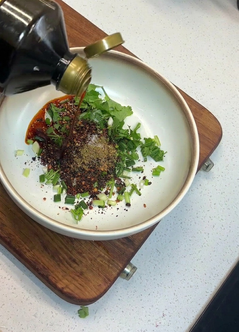 Mano vertiendo salsa de soja desde una botella de cristal al cuenco con los ingredientes.