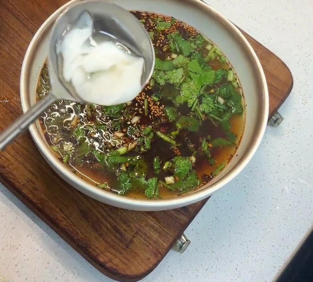 Cucharón con una porción de manteca de cerdo blanca introduciéndose en el caldo caliente.