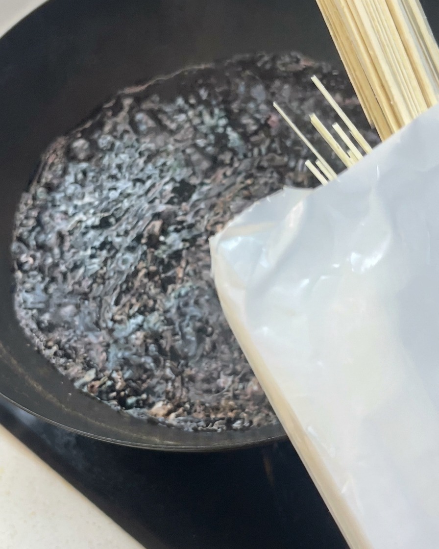 Fideos blancos secos introduciéndose en un wok con agua hirviendo.