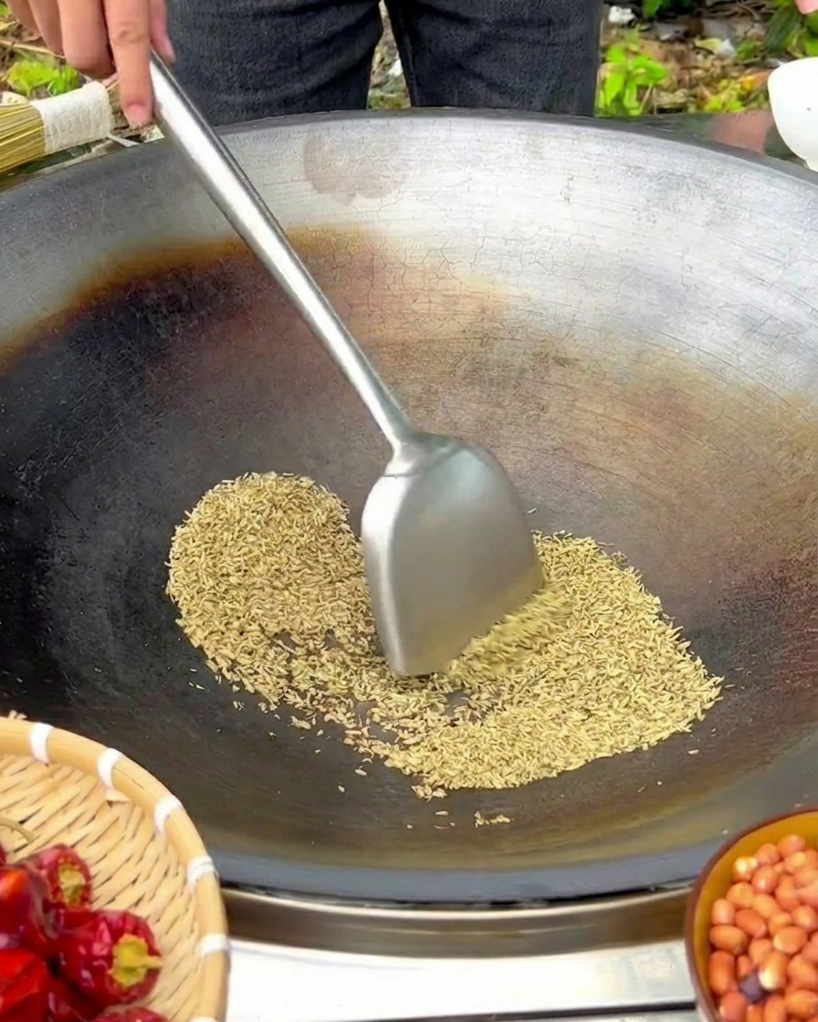 Semillas de hinojo removidas con una espátula de metal en un wok de hierro sobre fuego bajo.