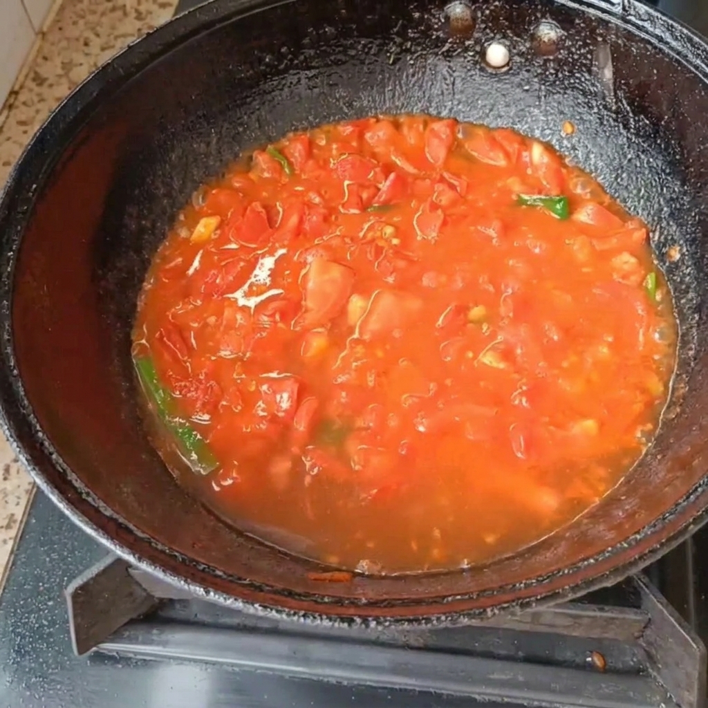 Tomates picados y cebolletas hirviendo en agua dentro de un wok negro en una cocina de gas.