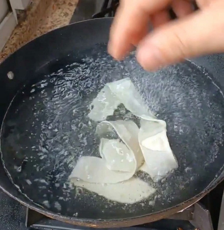 Cintas de fideos anchos y hojas de verdura siendo sumergidas en una olla de agua hirviendo.