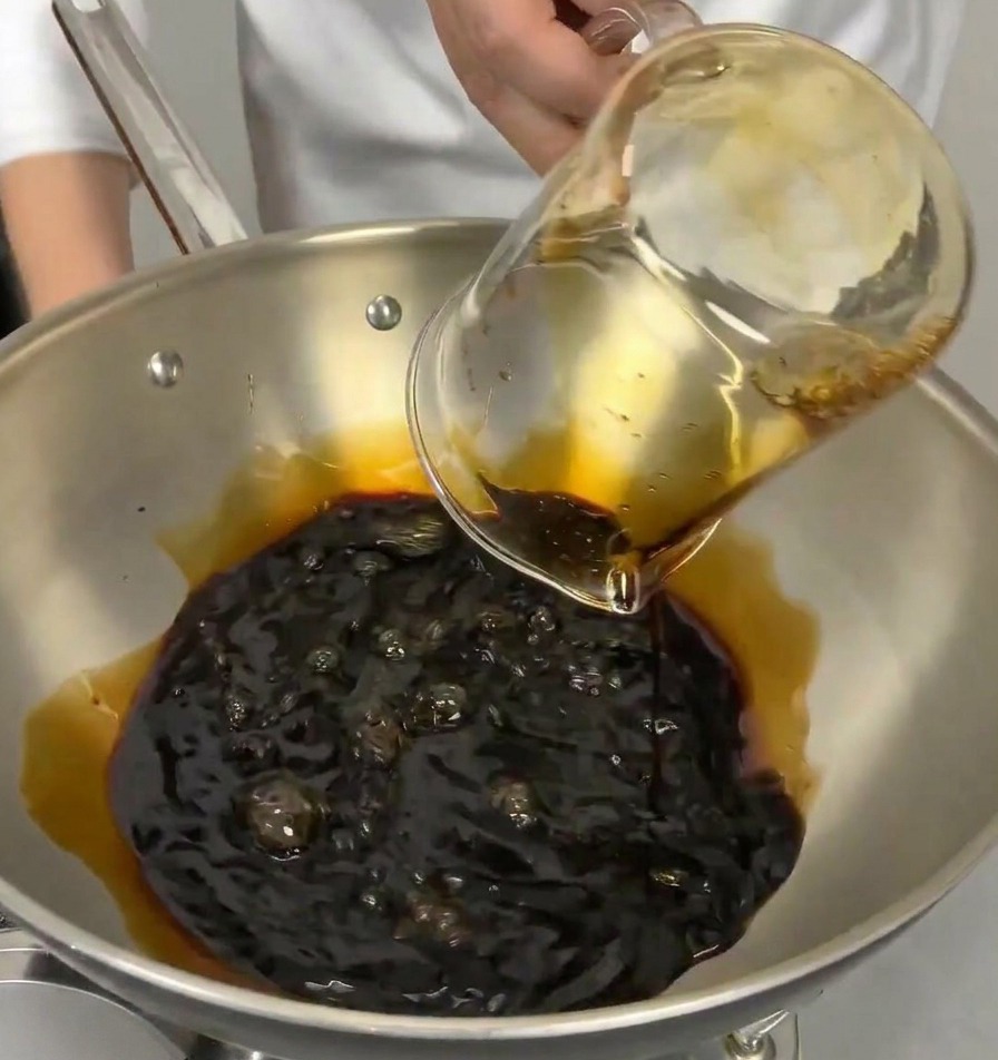Una jarra medidora vertiendo vino de cocina japonés transparente en una cacerola que contiene salsa de soja oscura.
