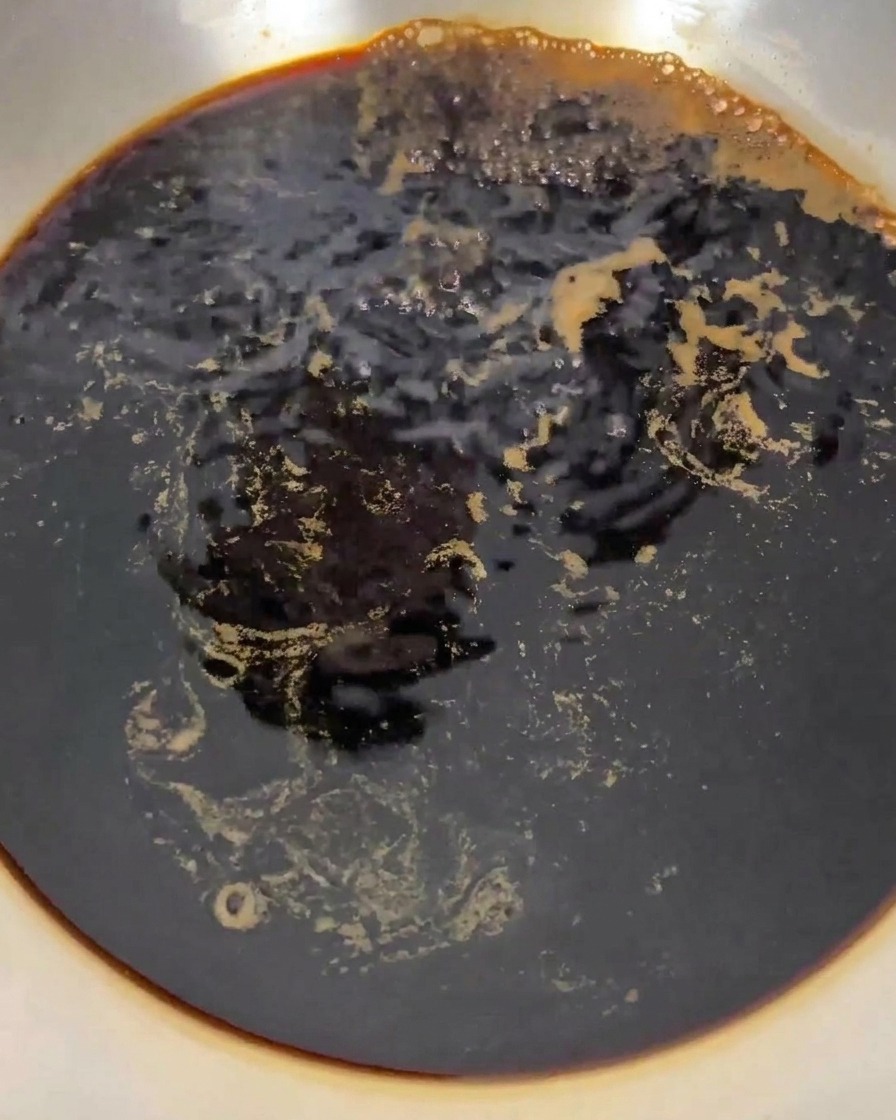 La mezcla de líquido oscuro burbujeando y hirviendo vigorosamente en una cacerola de acero inoxidable sobre el fuego.