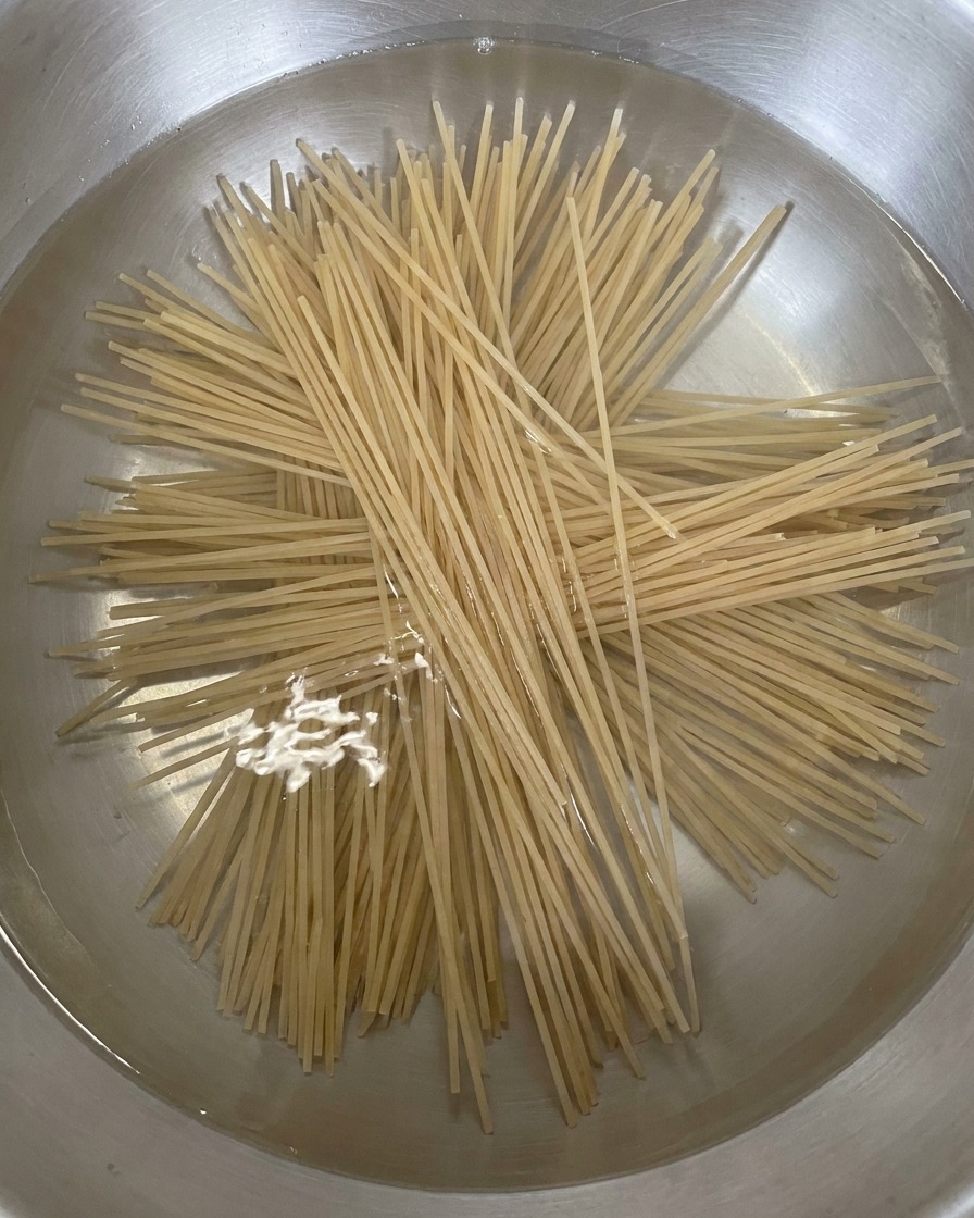 Fideos soba secos y rectos añadiéndose a una olla de agua hirviendo, extendiéndose en forma de estrella.