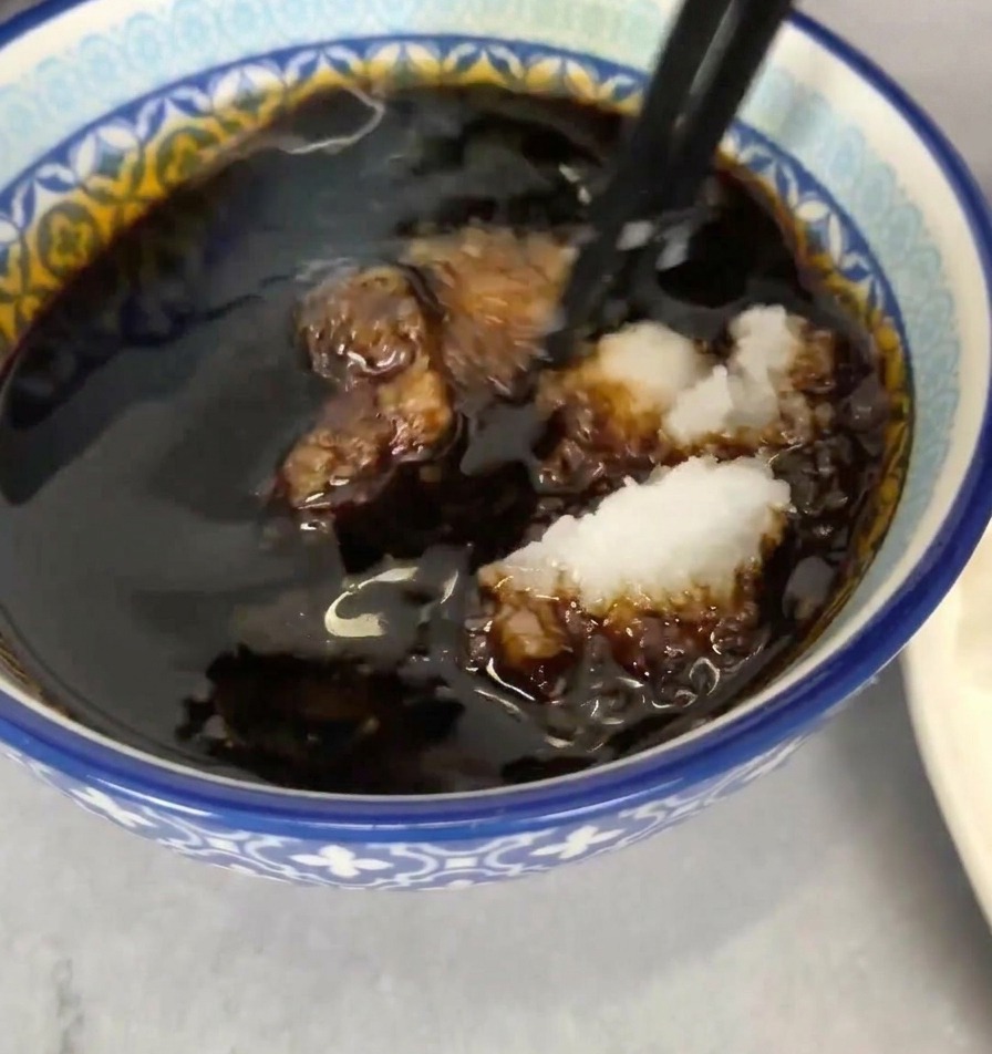 Un bol azul y blanco lleno de salsa oscura, con una porción de rábano rallado siendo mezclada con palillos negros.