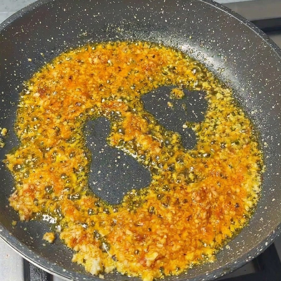 Carne de cerdo picada siendo removida en una sartén con una base de ajo picado y pasta de camarones.
