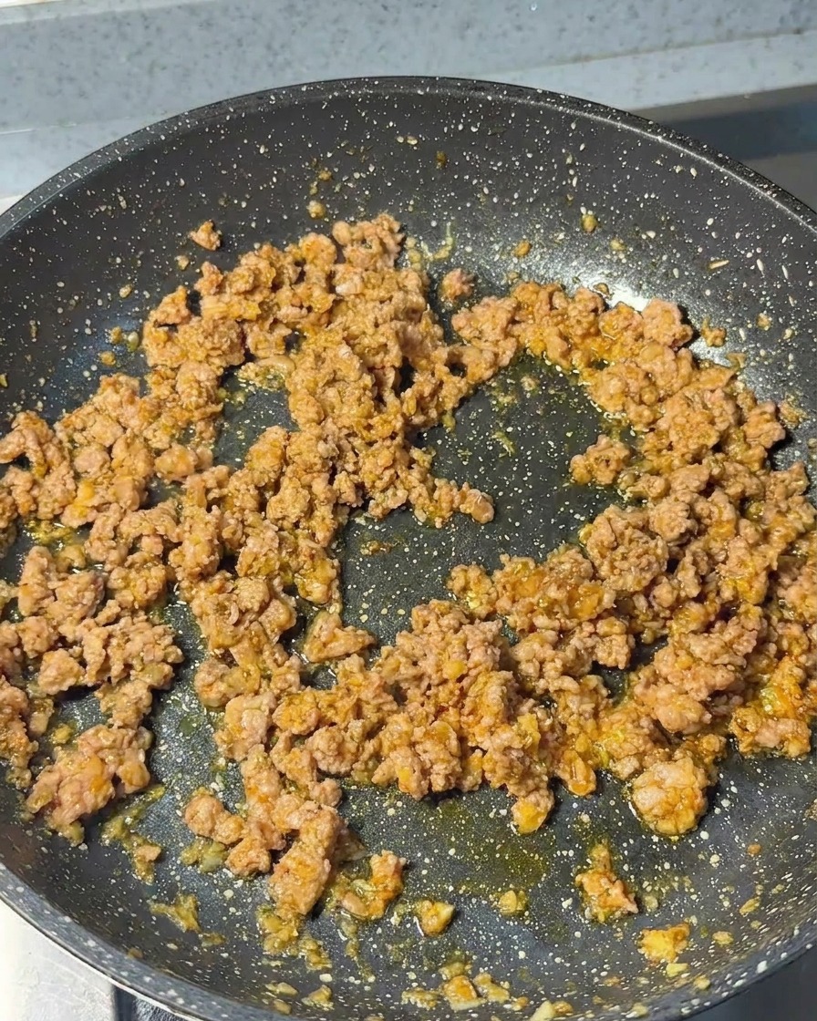Carne de cerdo picada salteándose en una sartén con aromáticos, mostrando una textura dorada y desmenuzada.