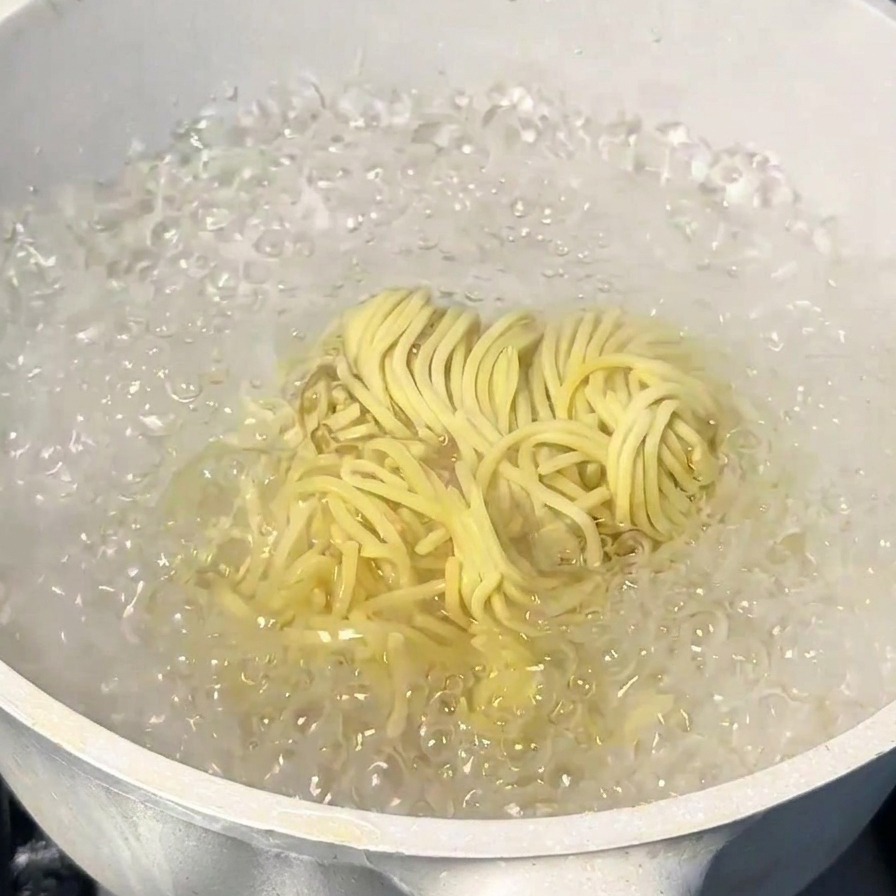 Un manojo de fideos ramen amarillos cocinándose en una olla con agua hirviendo vigorosamente.