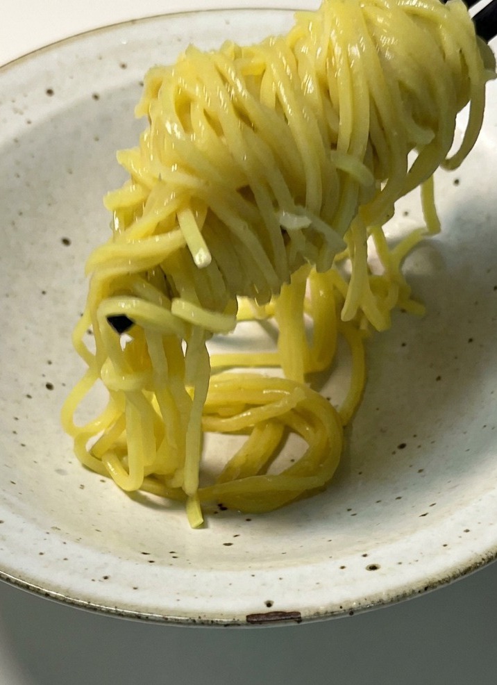 Fideos amarillos cocidos siendo levantados con palillos y colocados en un bol de cerámica de color claro.